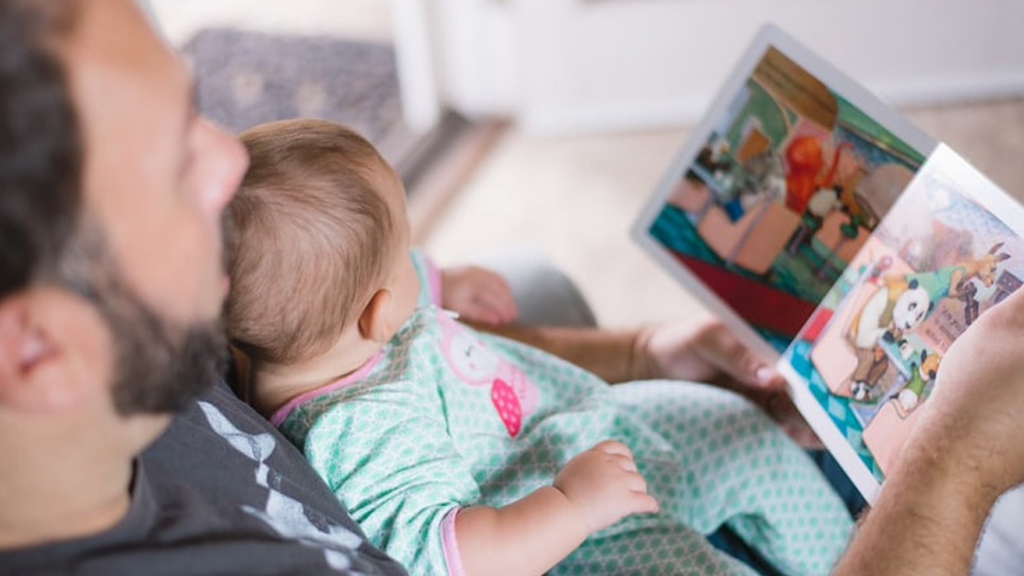 Photo of a father reading a book to a small infant being held in his arms