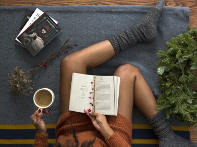 Woman sits reading books wearing cozy socks and with a cup of coffee in hand