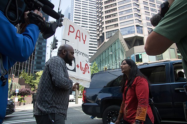 organizing: A Seattle-based rideshare worker speaks to a passerby about the ills of gig work and worker demands for pay transparency. Credit: Wikimedia Commons