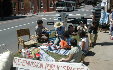 Picture of neighbors coming together with sign reading "re-envision public spaces"
